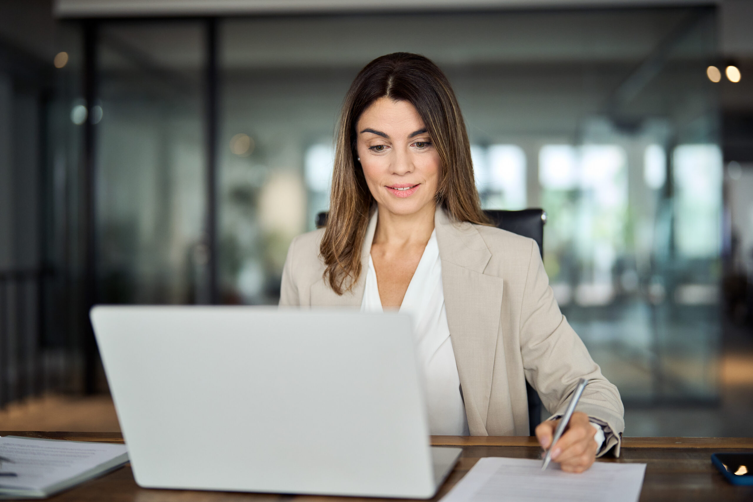 Anwältin mittleren Alters arbeitet im Büro am Laptop und schreibt. Symbolisiert eine 40-jährige weibliche Führungskraft, die sich über die Ergebnisse ihres Online Marketings freut.