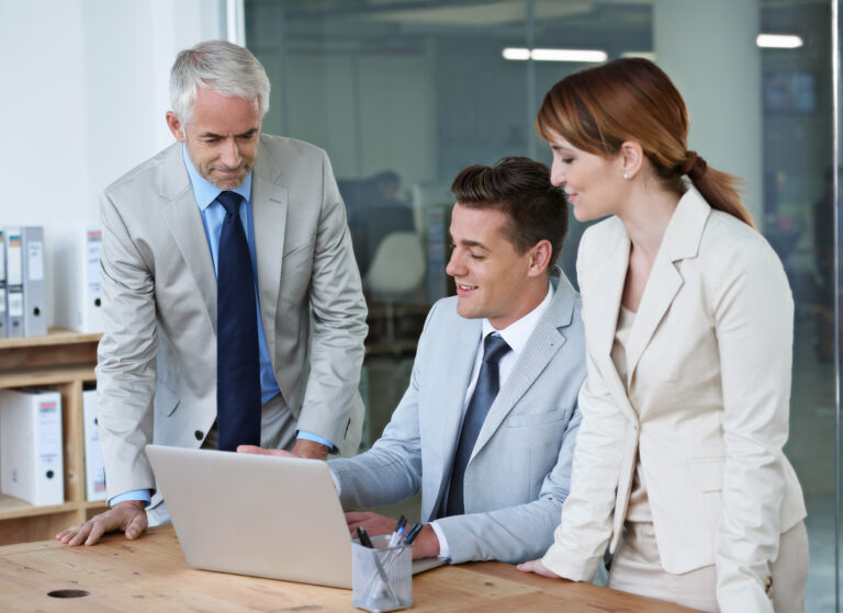 Drei Geschäftspersonen im Gespräch vor einem Laptop. Repräsentieren einen Anwalt, der sich mit ein Team von Webdesignern und Online-Marketing-Experten bespricht.